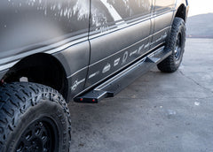 Side view of ROAMBUILT Flat Side Step in black textured aluminum, mounted on a Mercedes Sprinter, showing raised grip edge and lights.
