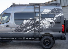Full view of ROAMBUILT Flatpack Ladder mounted on a Mercedes Sprinter van, showing all-aluminum construction and wide, notched traction steps.