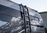 Middle-to-top view of ROAMBUILT Flatpack Ladder mounted on Mercedes Sprinter van, showing wide notched steps and aluminum side rails.