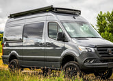 Passenger side view of SafariRack 2.0 SLB mounted on a 2007+ Mercedes Sprinter van, showing curved front profile, perforated decking, and rugged aluminum design.