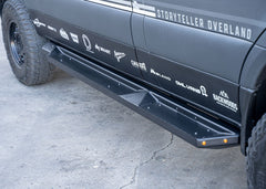 Front-to-back passenger side view of ROAMBUILT Flat Side Step on Mercedes Sprinter, showing black aluminum finish and integrated and small lights.