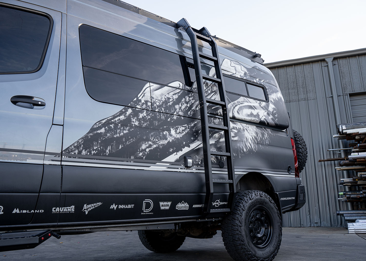 Side profile view from bottom to top of the ROAMBUILT Flatpack Ladder mounted on a Mercedes Sprinter, looking upward to show full height and attachment points.