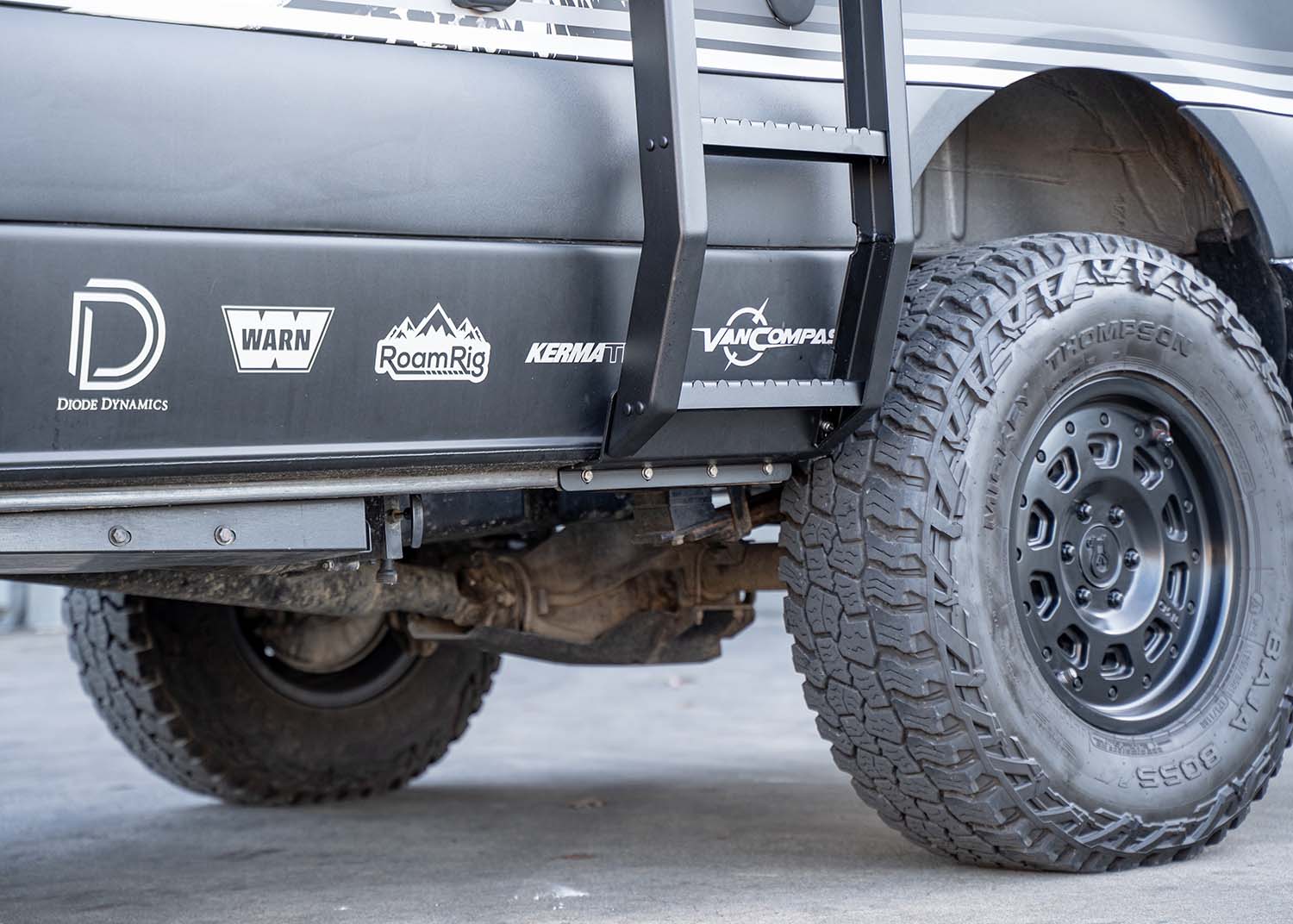 Close-up view of the bottom of the ROAMBUILT Flatpack Ladder mounted to the Mercedes Sprinter pinch weld, showing secure hardware and attachment point.