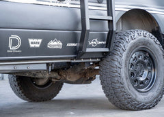 Close-up view of the bottom of the ROAMBUILT Flatpack Ladder mounted to the Mercedes Sprinter pinch weld, showing secure hardware and attachment point.