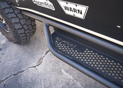 Close-up view looking down at the rear section of the ROAMBUILT Passenger Side Tube Step, highlighting the logo and perforated tread surface.