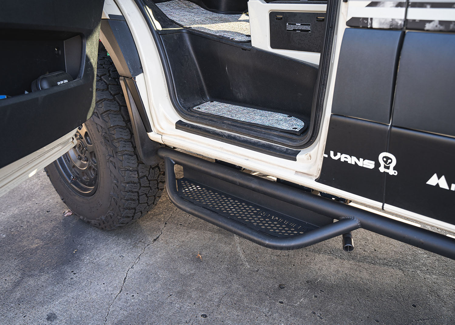 Driver side rear-to-front view of ROAMBUILT Mercedes Sprinter Side Step mounted beneath the van, highlighting full-length perforated aluminum decking for traction and visibility.