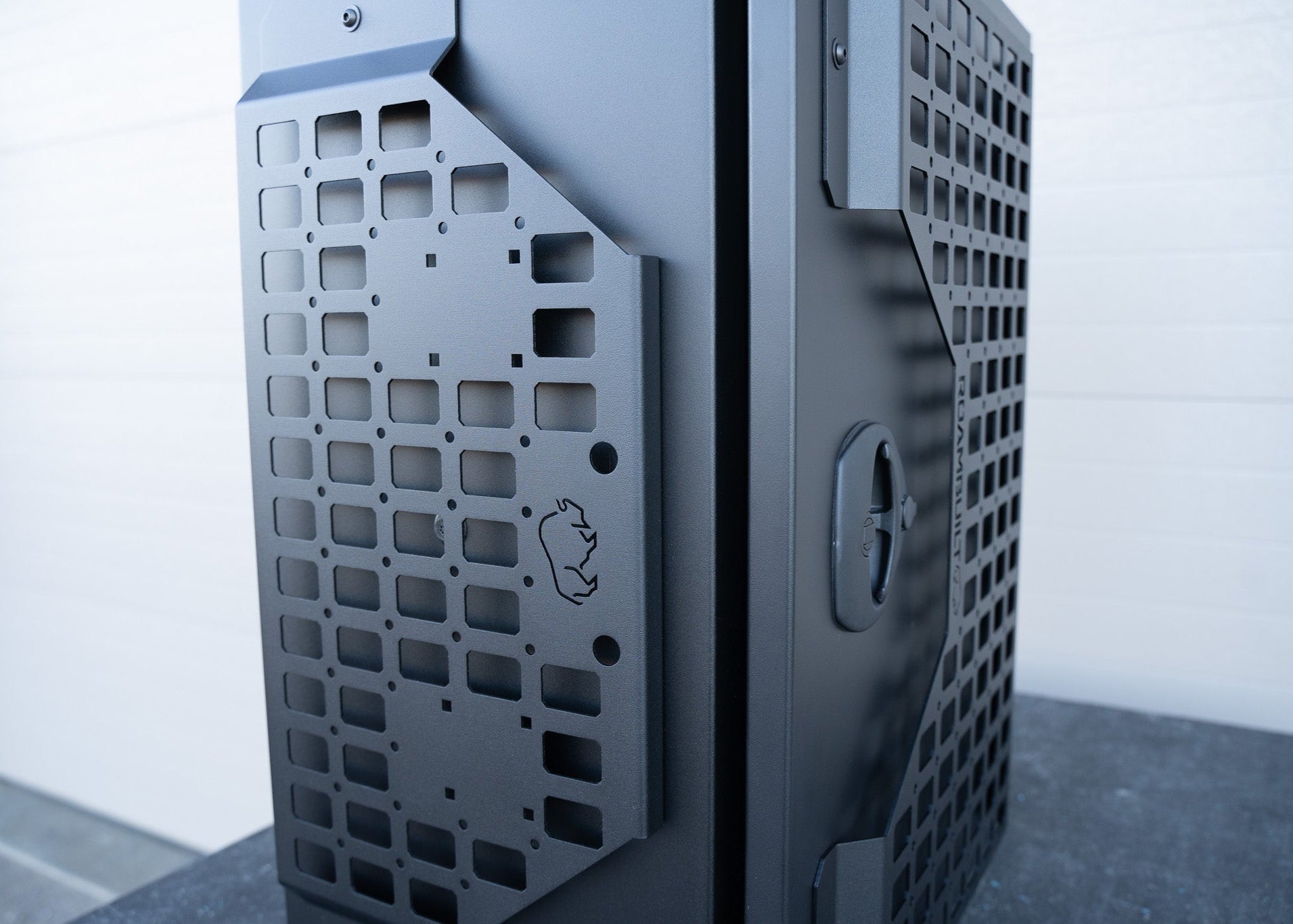 Close-up side profile of the ROAMBUILT Universal Aluminum Storage Box showing the black semi-textured powder-coated exterior, molle panels, and sturdy door latch mechanism.