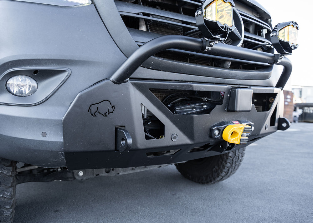 Passenger side profile close-up of the ROAMBUILT LoPro Front Bumper on a Mercedes-Benz Sprinter van, highlighting integrated steel shackle mounts, a winch mounted within the steel cradle, and Baja lights mounted to the welded aluminum bull bar, all encased within a lightweight aluminum shell.