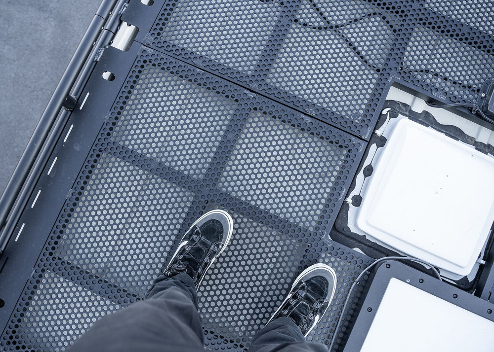 Top view close-up of the ROAMBUILT Safari 2.0 roof rack connection point, showing the secure bolt-on hardware and sturdy 5052 aluminum construction.