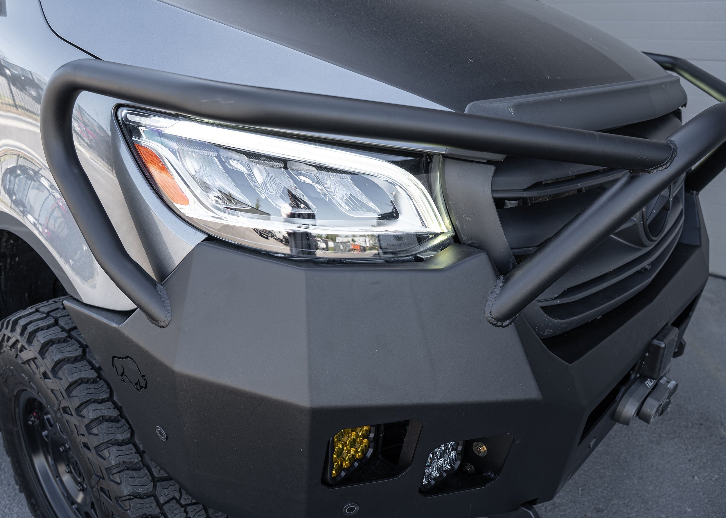 Top-side passenger view of a Mercedes Sprinter van featuring the Full Guard Front Bumper, showcasing its contoured fit, hybrid steel and aluminum build, and detailed design elements like light pockets and winch mount for robust, lightweight front-end protection