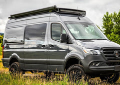 Passenger side view of SafariRack 2.0 SLB mounted on a 2007+ Mercedes Sprinter van, showing curved front profile, perforated decking, and rugged aluminum design.