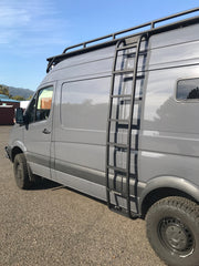 Driver side view of a Mercedes Sprinter van with the full ROAMBUILT Straight Side Ladder mounted, showing the complete ladder length, mounting brackets, and integration with the vehicle’s roof rail and body.