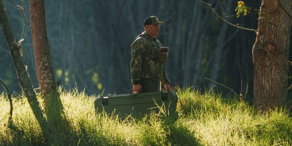 [A0030-MMAN-GRN] @expanded A man in camo walking through the woods, carrying his Ranger Green Honcho 80 D-co case that he uses for his bow.