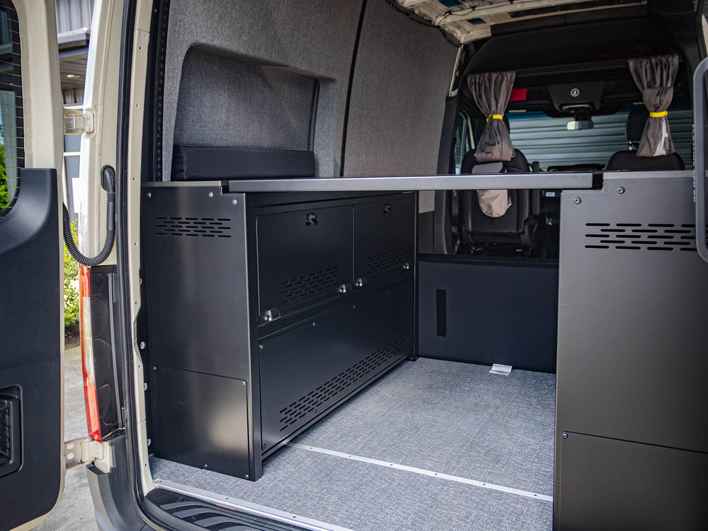 Angled view of installed Modular Cabinet Bed System for Sprinter & Transit in East-West orientation from rear of van, showing cabinet doors and fixed panel in use