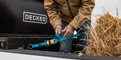 @expanded [ATB-DRING] Person securing a bale of hay with a blue strap next to a DECKED'Tool Box.