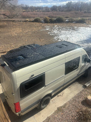 Drone view of entire van roof equipped with ROAMBUILT deck panels, set up for storage and lounging, showcasing full rooftop utility and layout.