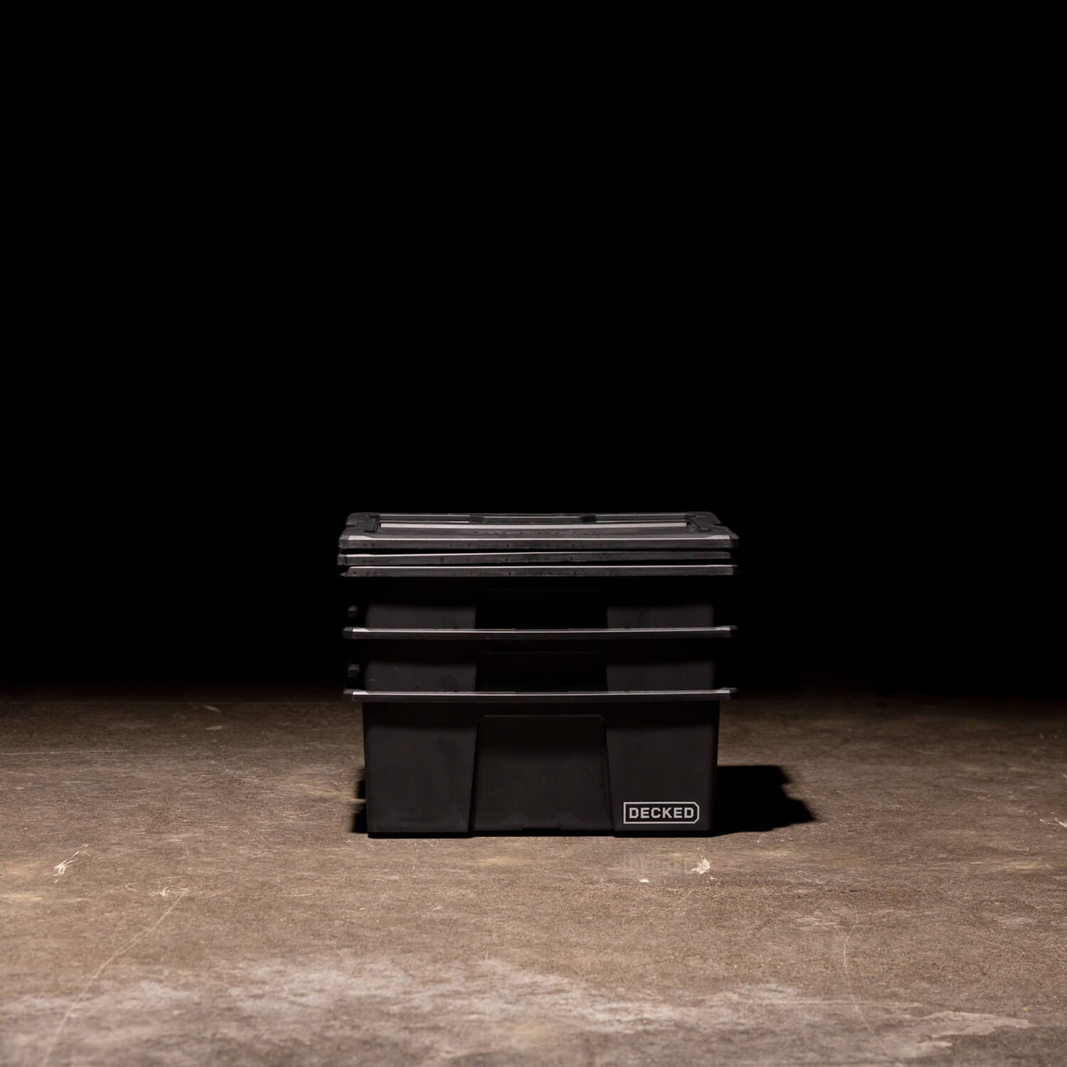 [A0041-DBIN-BLK, A0040-DBIN-BLK] Three black Payloader Bins nested together with the lids sitting on top in a garage with a dark, shadowy background.