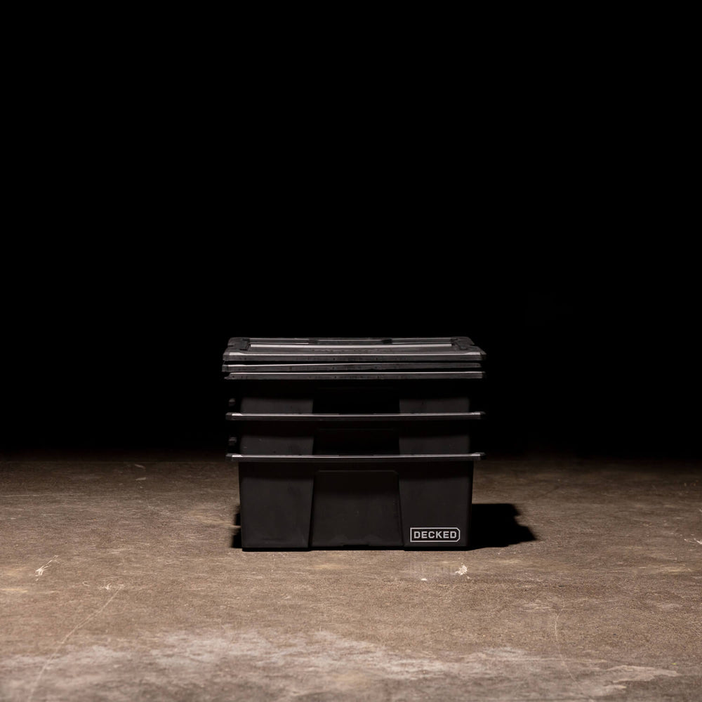 [A0041-DBIN-BLK, A0040-DBIN-BLK] Three black Payloader Bins nested together with the lids sitting on top in a garage with a dark, shadowy background.
