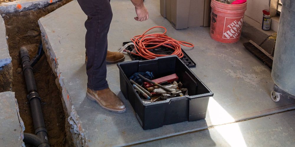 [A0041-DBIN-BLK, A0040-DBIN-BLK] @expanded A man at a jobsite retrieving tools and extension cords from a black Payloader Bin.