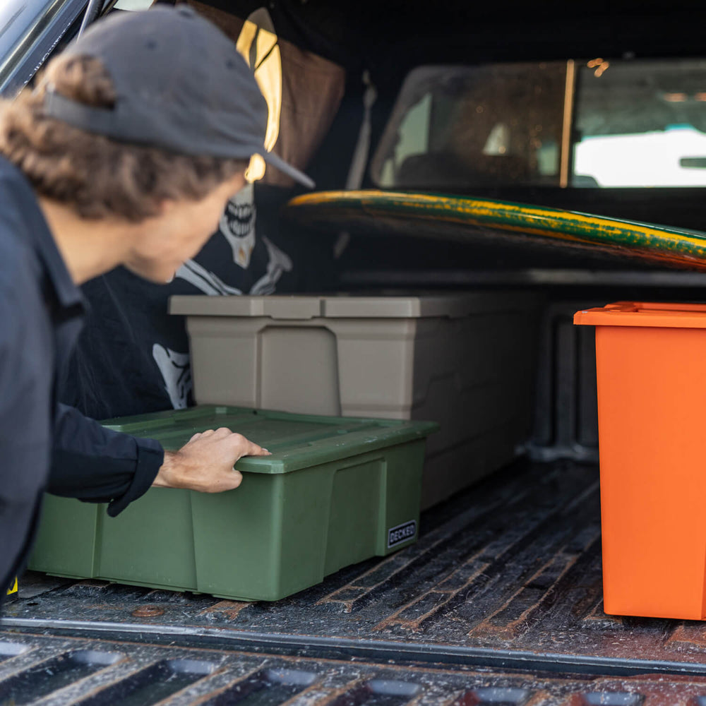 [A0041-DBIN-GRN, A0040-DBIN-GRN] A man loading Payloader Bins into the bed of his truck along with a surfboard for a day on the water.
