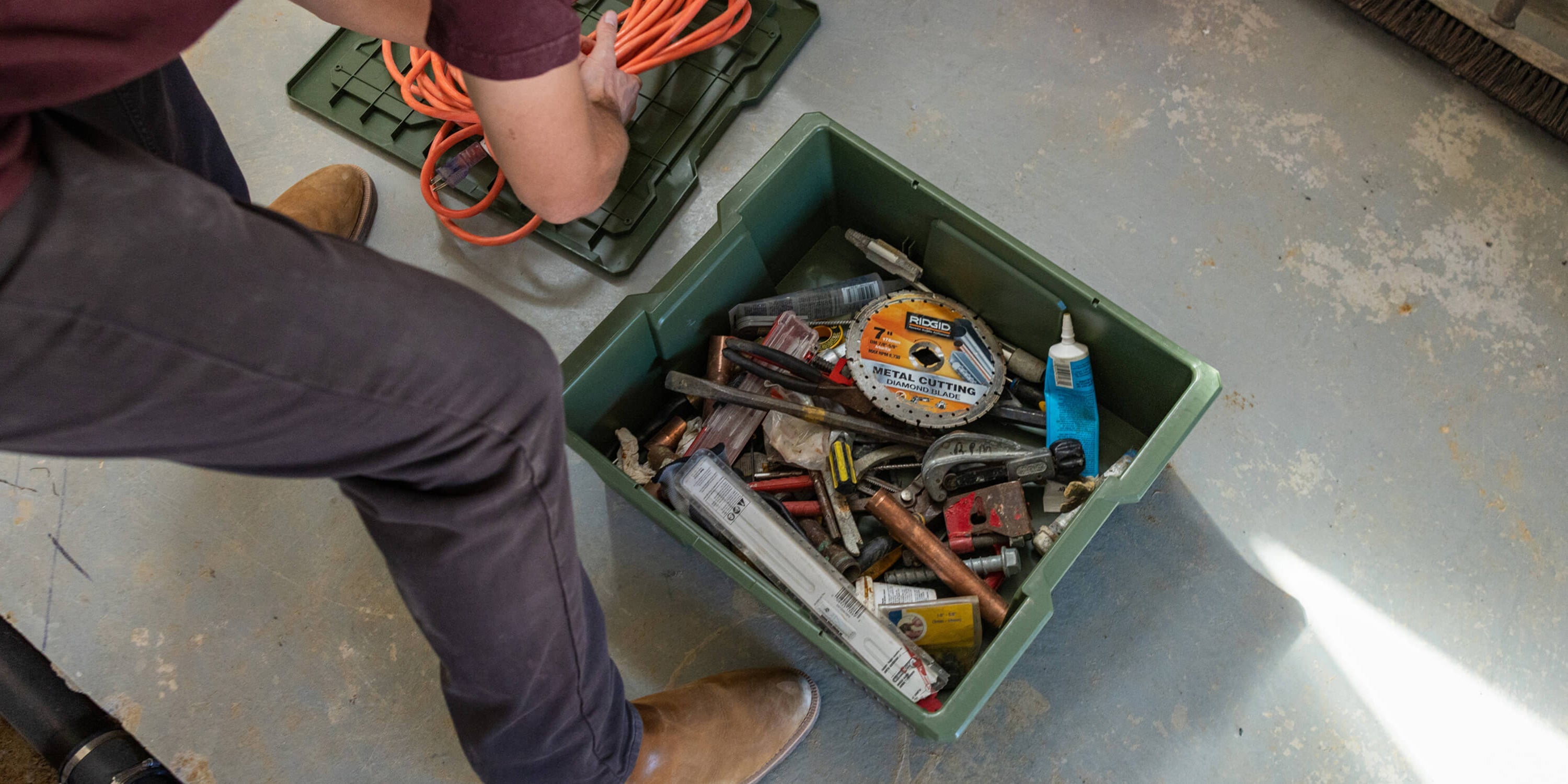 [A0041-DBIN-GRN, A0040-DBIN-GRN] @expanded Person organizing extension cords and tools in a ranger green Payloader bin on a concrete floor.
