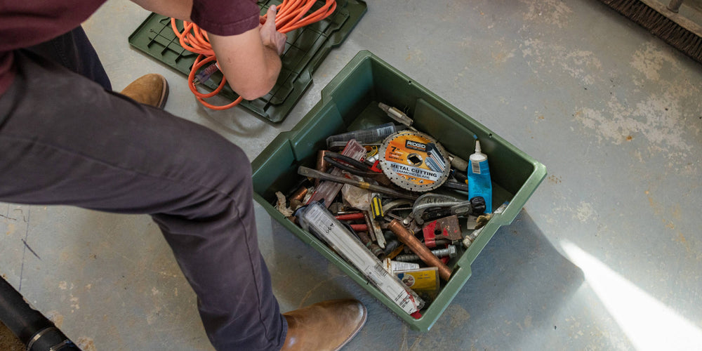 [A0041-DBIN-GRN, A0040-DBIN-GRN] @expanded Person organizing extension cords and tools in a ranger green Payloader bin on a concrete floor.