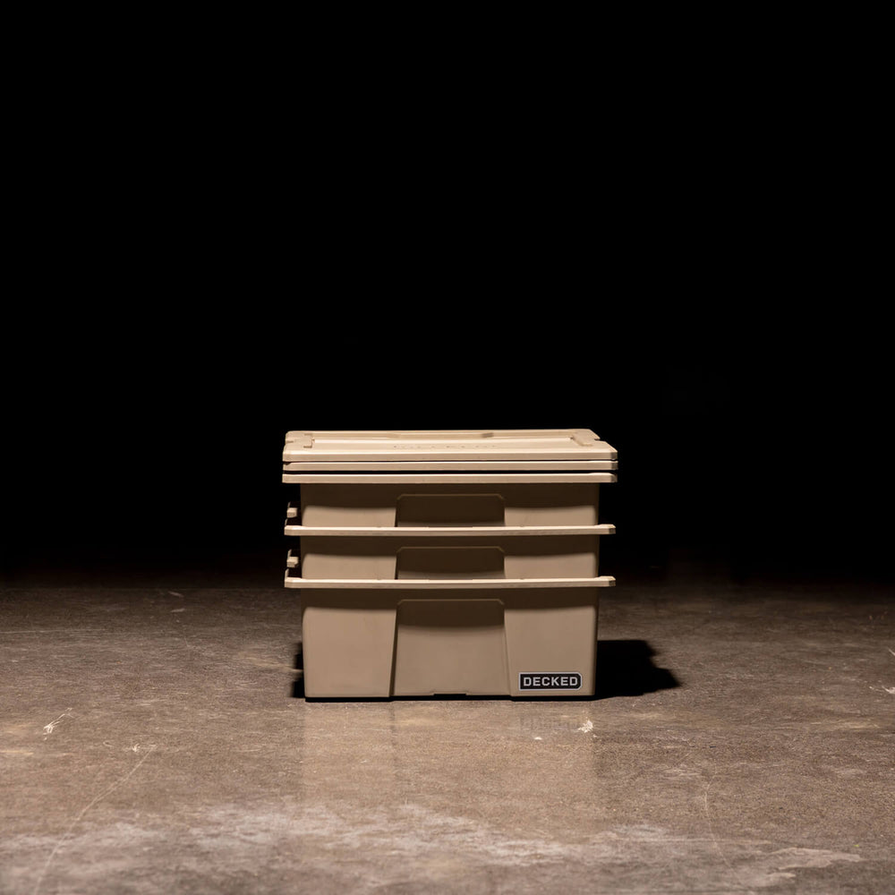 [A0041-DBIN-TAN, A0040-DBIN-TAN] Three desert tan Payloader Bins nested together with the lids sitting on top in a garage with a dark, shadowy background.