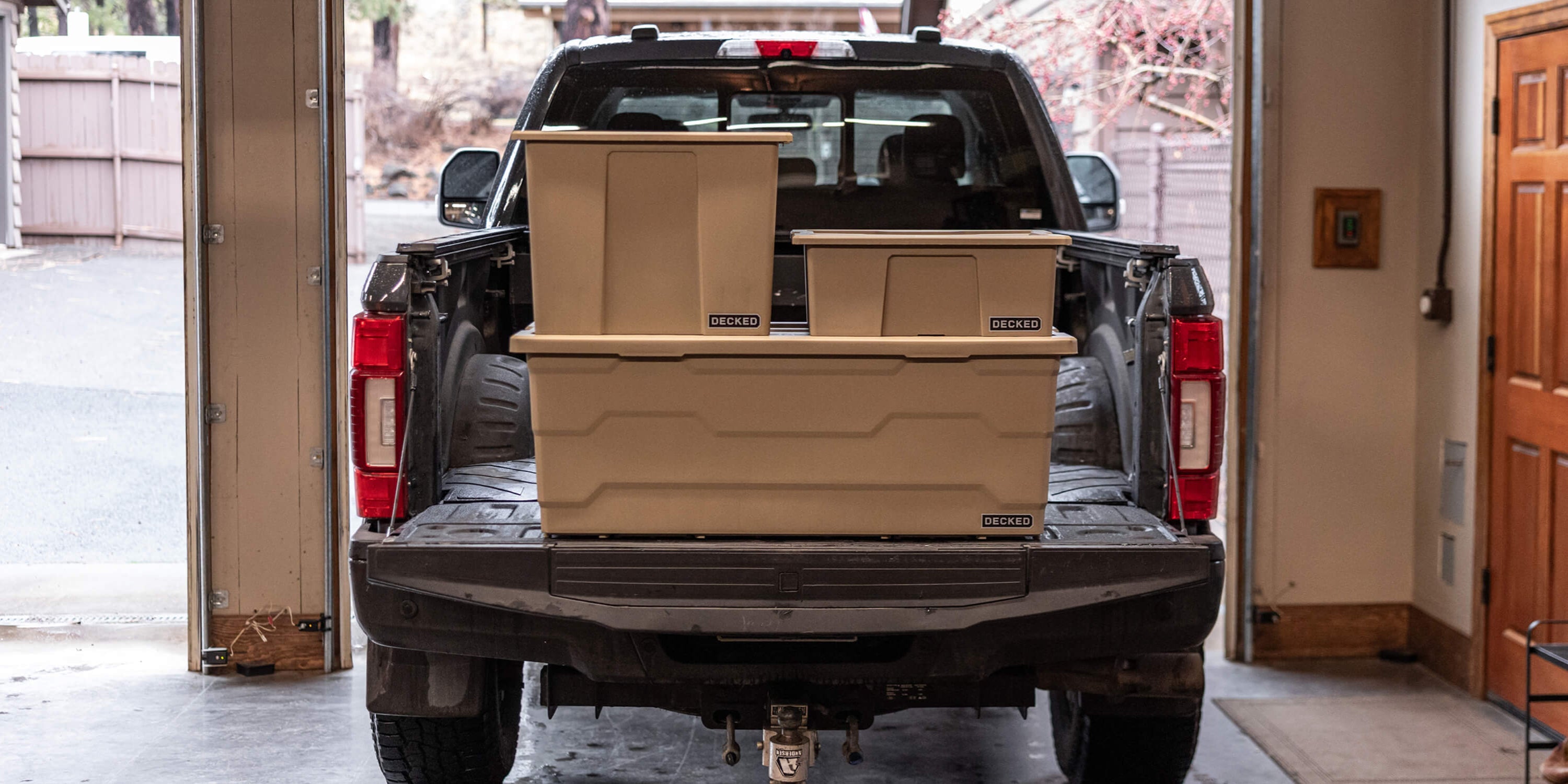 [A0041-DBIN-TAN] @expanded The three desert tan Payloader sizes stacked on the tailgate of a truck in a garage.