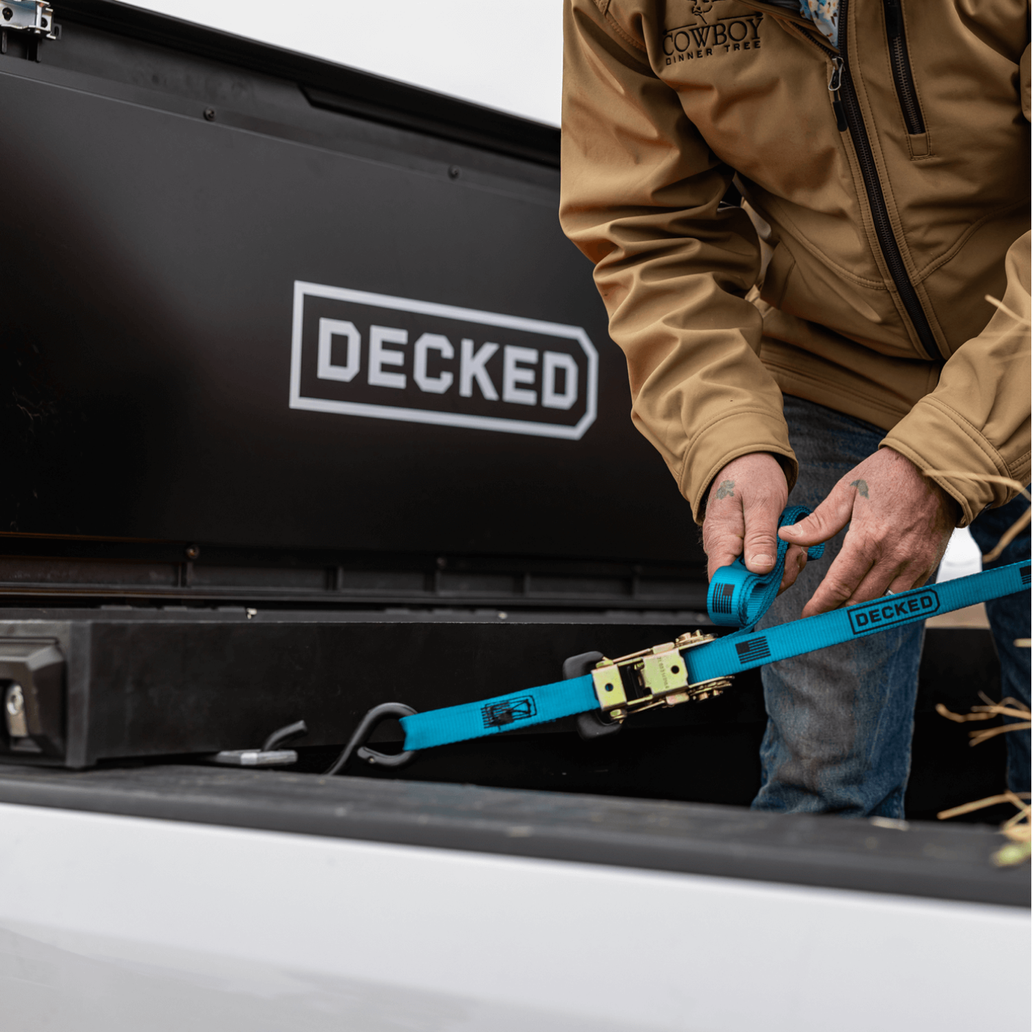 [DTB2-BLK, DTB2T22-BLK] Person securing a DECKED blue Ratchet Strap to their DECKED Tool Box in order to lash down the cargo in their truck bed.