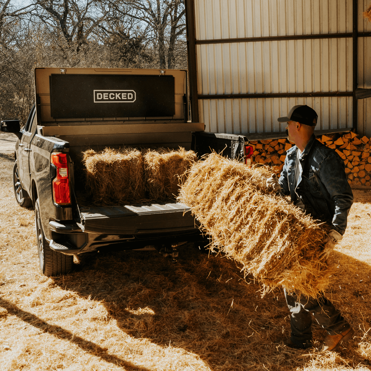 [DTB2-TAN, DTB2T22-TAN] Person loading hay bales into a truck with 'DECKED' Tool Box in the bed.