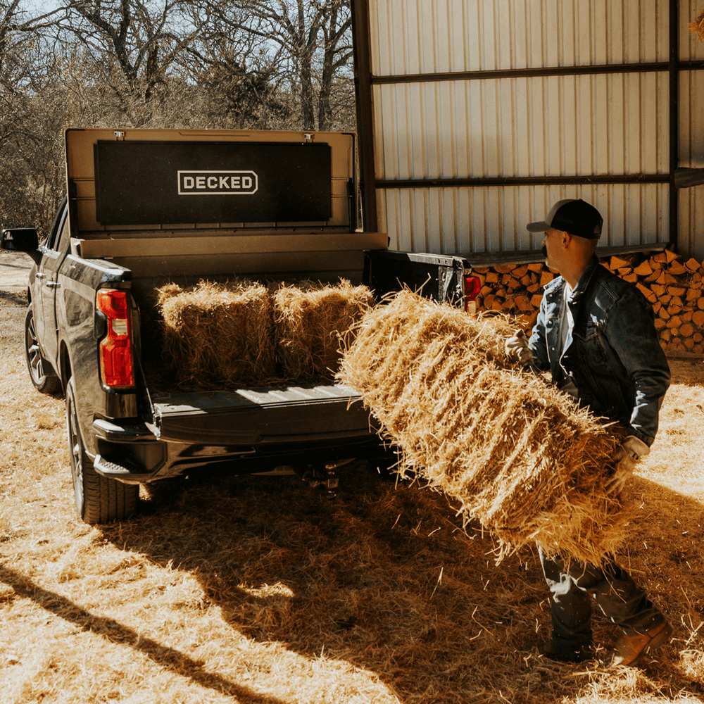[DTB2-TAN, DTB2T22-TAN] Person loading hay bales into a truck with 'DECKED' Tool Box in the bed.